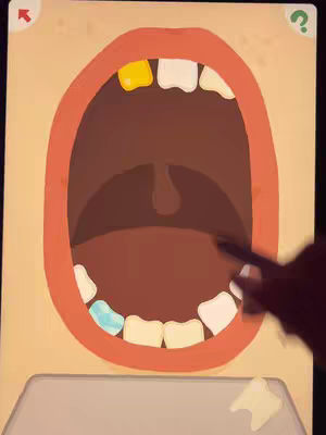The image shows a close-up view of a mouth, drawn in a cartoon style, with teeth and gums visible. The teeth are various colors, with one gold tooth and one blue tooth. A black stylus is held near the teeth. The background is a pale tan color, suggesting a game interface.