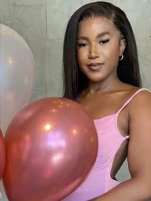 A woman with long black hair wears a pink top and holds a large red balloon. In the background, another white balloon can be seen. The image has a soft, glowing effect.