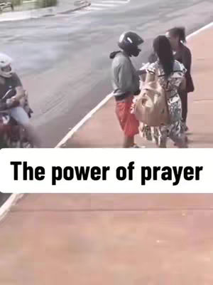 The image shows a street scene with a person on a motorcycle on the extreme left and a group of three people standing on the right side of the frame. A text box with the phrase, 'The power of prayer,' is overlayed at the bottom, highlighting the overall focus on faith.