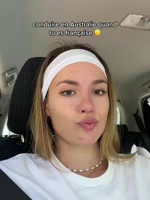 A young woman with blonde hair and a white headband is seated in the driver's seat of a car. Text overlays the top of the image. Her expression is neutral with a slight pout.