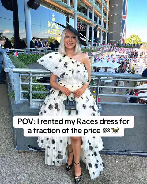 A woman in a white dress with large black polka dots and a wide-brimmed hat stands outside a building. The background shows a racecourse with flags and people. A text overlay reads 'POV: I rented my Races dress for a fraction of the price.'
