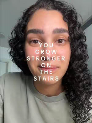 A close-up shot of a woman with curly black hair. She is wearing a light green shirt and her face takes up most of the frame. Text overlayed on her face reads: 'You grow stronger on the stairs.'