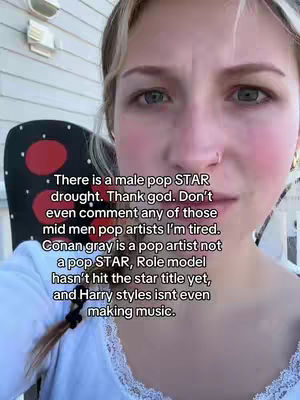 A close-up shot of a young woman with fair skin and blonde hair, looking directly at the camera with a slight frown. The text overlayed discusses male pop music artists.