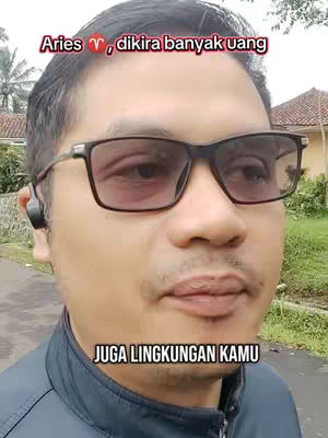 A man with dark hair and glasses is the main subject. The background appears to be a residential area with buildings and greenery. Text is overlaid on the image. The color palette is natural with the man wearing a black jacket. The composition is a selfie-style shot focusing on the subject's face.