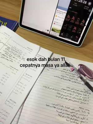 The image shows a workspace with open notebooks filled with handwritten notes in Arabic, a tablet displaying a timer and app icons, and a pen. The composition is top-down. Text overlays are present.