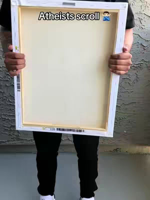 A person holding a blank canvas, with the canvas itself taking up most of the frame. The person's lower body is visible, wearing black pants and white shoes. The canvas is white, and the person is standing outside by some siding.