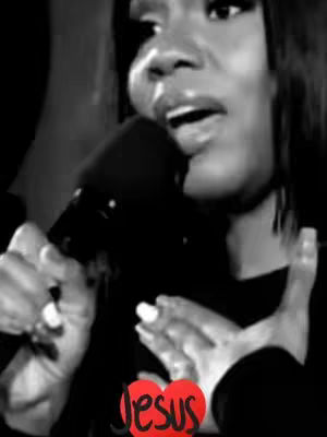 A black and white image featuring a woman with dark hair, holding a microphone. Her mouth is open as she speaks into the mic. A red heart graphic with the word 'Jesus' is overlaid at the bottom.
