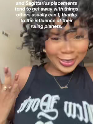 A woman with curly hair, wearing a black tank top, smiles broadly, with text overlayed indicating astrological content. The background is neutral, drawing focus to the woman.