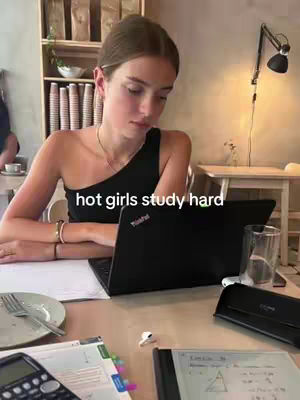 A young woman is sitting at a table in a cafe, studying with a laptop and various study materials. Text overlayed at the top.