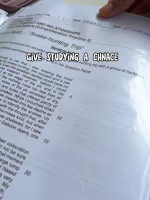 The image shows an open book with text and handwriting, a hand is casually holding the top right corner of the paper. The text is centered and has an overlay 'GIVE STUDYING A CHNACE'