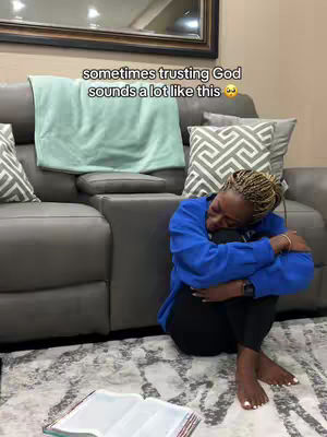 A woman is sitting on the floor, leaning against a gray couch. She is dressed in a blue sweater and black pants and has short, blonde hair. She is holding her knees close to her chest. In front of her on the floor is a bible. Above her head is a light green blanket draped over the back of the couch. The text is overlaid on the cover image.