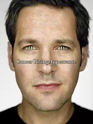 Close-up of a fair-skinned man with short, dark hair, green eyes, and a neutral expression. Text overlayed across the image reads "Cancer Rising Appearance".