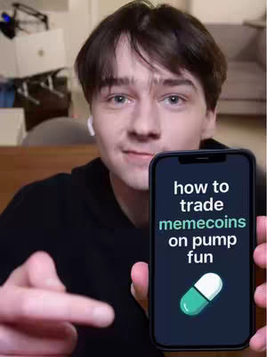 A young man with short brown hair is centered in the frame, holding a smartphone. The phone's screen displays the text "how to trade memecoins on pump fun" over a dark background, with a graphic of a capsule pill above the text. The man is smiling slightly, looking towards the camera with a friendly expression. He's wearing a black hoodie and a white earbud is visible in his left ear. The background is blurred, suggesting a home setting with items like a laptop and lamps.