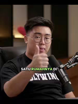 A man wearing glasses and a black shirt is giving a thumbs up while talking. The cover image has a black background and the text "SATU RUMAHNYA DI" is overlaid.