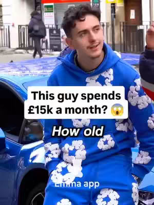 A young man in a blue hoodie stands in front of a blue car, posing for the camera. Text overlays appear on the image, and the background shows a street scene.