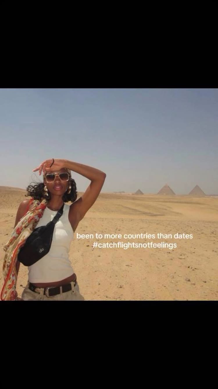 A woman in sunglasses stands in a desert landscape with the Pyramids in the background. She holds up her hand to shield the sun, wearing a white tank top and a fanny pack. Text overlay reads 'Been to more countries than dates' and '#catchflightsnotfeelings'.