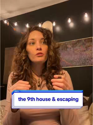 A woman with long curly brown hair is centered in the frame, gesturing with her hands while speaking. She's wearing a light-colored top with a necklace. Behind her, a dark wall is seen with soft lighting from string lights and a framed picture. A graphic overlay at the bottom reads: 'the 9th house & escaping'.
