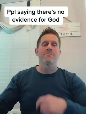 A man is centered in the frame, looking slightly towards the upper left. Above his head is a white rectangular overlay with black text. Behind him is a white wall.  The man is wearing a dark blue long-sleeve shirt. His face is in focus.