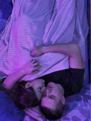 A close-up shot of two people lying down, presumably in bed. They are embracing, with their faces close together, suggesting intimacy. The lighting is soft, with a purple hue, giving a romantic feel. The composition is intimate, focusing on the connection between the two individuals.