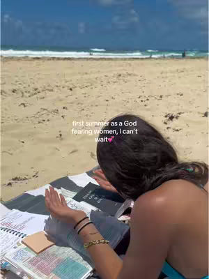 A woman is relaxing on a beach, studying with a Bible open in front of her. She's reaching her hands towards the sky and there's a beach scene behind her.