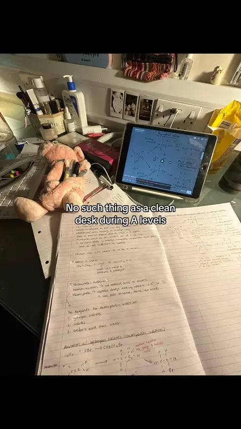 A messy desk with notebooks, a tablet showing chemistry notes, and a stuffed animal.