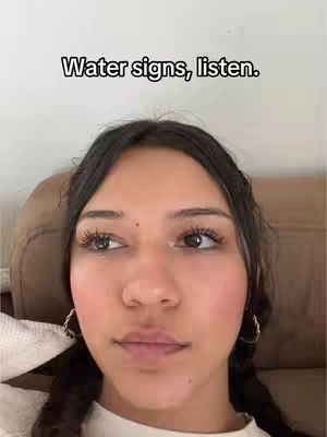The cover image shows a close-up of a young woman's face. She has dark hair pulled back, large brown eyes with long eyelashes, and is wearing hoop earrings. She is looking to the side, and the background appears to be a blurry brown. Text overlayed at the top reads, 'Water signs, listen.'