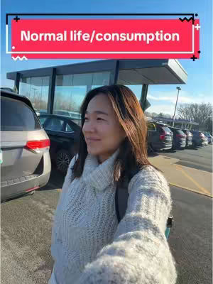 A woman in a light-colored outfit is standing outside near a car, with a parking lot and building visible in the background.