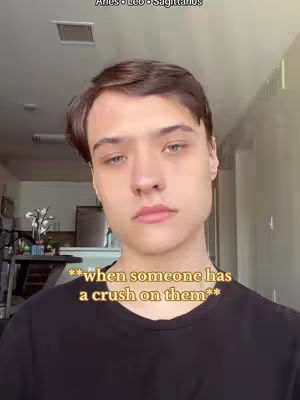 A young man with light skin, brown hair, and light eyes looks directly at the camera. He wears a black t-shirt and is positioned in front of a blurred indoor background. Text overlays appear at the top and bottom of the image.