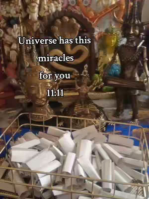 The cover image displays a collection of religious figurines and items, including statues, a golden head, and a basket filled with rolled white papers. Overlayed text reads "Universe has this miracles for you 11:11". The background is filled with various golden and ornate religious artifacts.