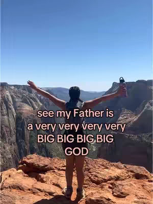 A woman stands on a rocky outcrop with her arms outstretched, appearing to embrace the scenic landscape views around her. She has dark hair in a cap. Text overlayed on the image reads, "see my Father is a very very very very BIG BIG BIG BIG GOD."