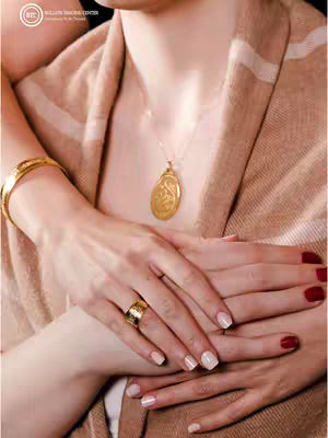 The cover image showcases a close-up shot of a woman's hands adorned with jewelry. Her hands are intertwined, and she is wearing a gold bracelet on her left wrist, a ring on her ring finger, and a necklace with a pendant. The background is out of focus, featuring a beige and white striped scarf or fabric. The overall composition suggests a focus on elegance and luxury.