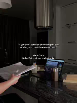 A dimly lit interior shot of a kitchen or workspace. A person's arm is holding a stack of papers in the foreground. Text overlays on the image provide a quote by Marie Curie.