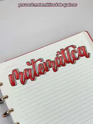 The cover image is a close-up of a notebook open to a blank page. Overlaid on the page is the word \"Matemática\" rendered in a vibrant, red, stylized font with a 3D shadow effect. The text \"pra você matemática é de qual cor\" is written in a smaller font above the main text. The background is muted.