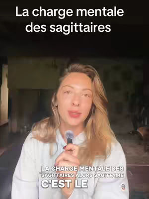 A woman with long, blonde hair is holding a microphone, centered in the frame. Above her is the text "La charge mentale des sagittaires" in large white letters overlaid on a dark background. Additional text is visible lower in the image, mentioning 'La charge mentale des sagittaires', beneath which is the phrase 'C'est le'. The lighting appears natural, and the background is softly blurred.