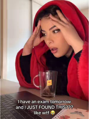 A woman wearing a red hooded robe sits at a desk, hands on her head, with an open laptop and a teacup in front of her. Text overlays the image.