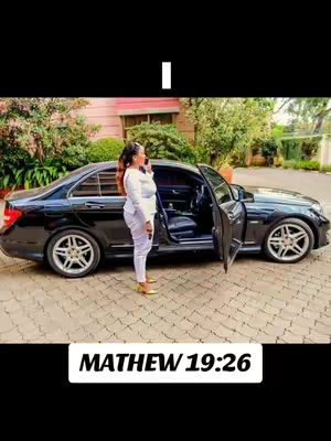 A woman in a white outfit stands next to a black car with an open door; text at the bottom says 'MATHEW 19:26'.
