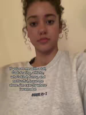 A young woman with curly hair, wearing a light-colored sweatshirt, looks at the camera. Text is overlaid on the image, listing qualities she seeks in a partner.