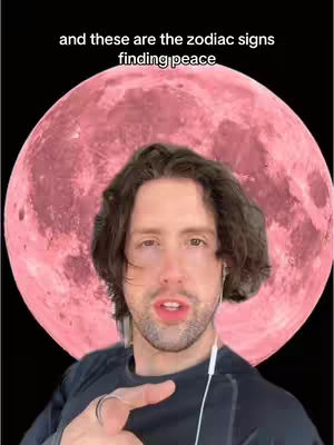 A medium shot features a man with short brown hair, centered in front of a large pink full moon. The man is pointing his right index finger towards the viewer. The background is solid black.