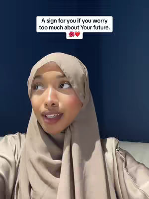 A woman wearing a hijab is the main subject, positioned against a dark blue background. Above her head, a white rectangle contains text. The woman has light skin and is looking slightly to her right. Her expression appears calm and reflective.