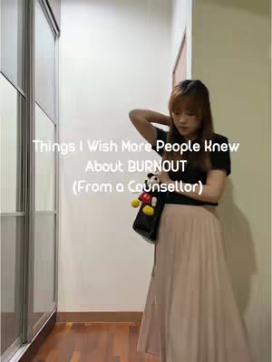 A woman stands in a well-lit hallway, dressed in a black top and a flowing beige skirt. She is leaning against a wall with her arm raised, hand near her head. She carries a bag with a Mickey Mouse accessory. Text overlayed on the image reads, 'Things I Wish More People Knew About BURNOUT (From a Counsellor)'.