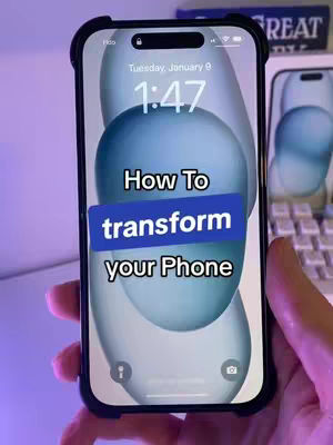 A hand holding an iPhone. The phone displays a lock screen with a pastel blue and white abstract background design. Overlayed on the screen is a text box with "How To transform your Phone" written inside it. The phone has a black case and the hand holding it is visible. The background shows items like a keyboard, a book.