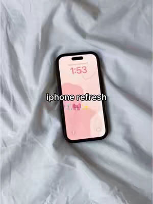 The image shows an iPhone on a white, textured surface, likely a bedsheet or blanket. The phone's screen displays a pink and white background with a stylized bow. The time 1:53 is visible at the top, and the caption 'iphone refresh' is overlaid in white text.
