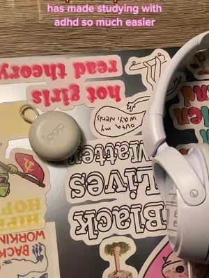 The image is a close-up shot of a laptop covered in colorful stickers, a pair of white headphones and a loop earplug case. A message is overlaid on top of the image. The colors present in this image are whites, pinks and neutral colors.