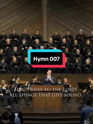 The cover image shows a live performance featuring a choir, an orchestra with string instruments, and a conductor. The choir and orchestra are positioned behind a central figure, the conductor. The background is a paneled wooden wall. Overlayed on the image is a black rectangle with white text that shows the number of the hymn.