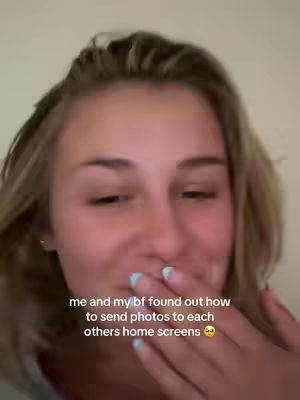 A close-up shot of a young woman with blonde hair. She's looking down and left, with a slight smile and her hand covering her mouth. Text overlaid on the picture reads, "me and my bf found out how to send photos to each others home screens" with a sad face emoji.