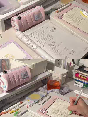 The cover image presents a top-down view of a study desk. Elements include a pink pencil case, open books with script, pens, and a glass of tea. The setting suggests a study environment, the color palette is soft with pink and beige tones.