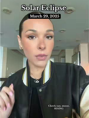 A woman in a black jacket with a white and yellow trim is the primary focus, with text overlays indicating a solar eclipse date. The background is a bright, well-lit room.