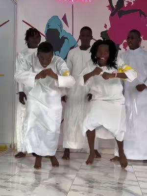 A group of six people, all wearing white outfits, are captured in a dynamic pose. The individuals are positioned in a room with a tiled floor and a wall that has a mural on it, the mural features abstract design elements in shades of blue and pink. The lighting seems to be from overhead sources. Two people in the front are centered in the shot.