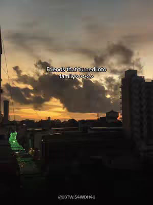 The cover image captures a cityscape at dusk or dawn, dominated by the silhouettes of buildings against a sky painted with warm hues of orange and grey. A text overlay reads "Friends that turned into family >>>>>" in a simple, readable font. The composition draws attention to the sky and text, conveying a sense of sentimentality and community.