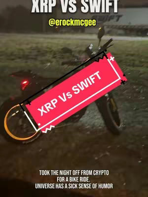 A night scene featuring an e-bike with a red and black overlay with text 'XRP Vs SWIFT'. In the background, there's a bike and dark surroundings, with a hint of headlights. The overall impression suggests a connection related to the crypto XRP and the transport company Swift with the text layout emphasizing the contrast.